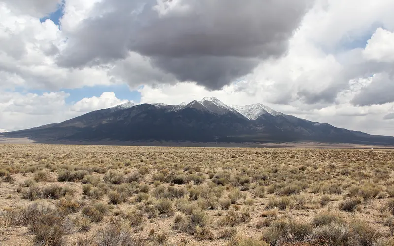desert scrub in foreground, spiky mountains in background, clouds