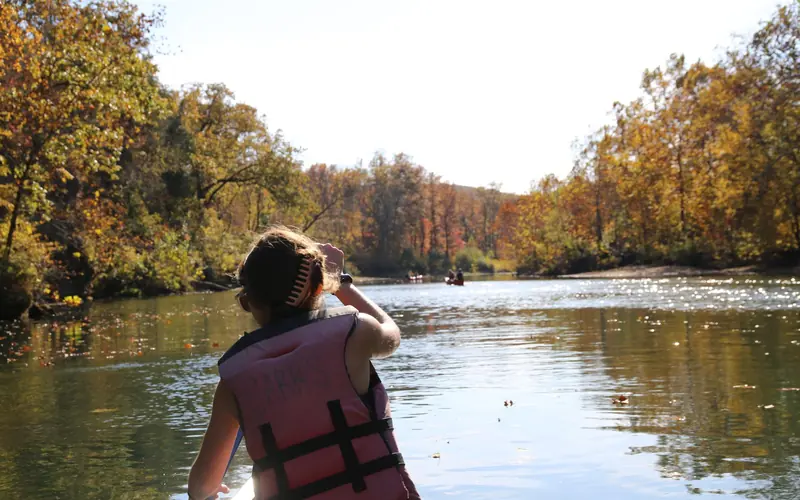 A woman paddles down a river while wearing a personal flotation device.