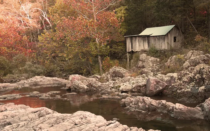 fall colors on leaves of trees surrounding a creek with an old wooden mill on the right