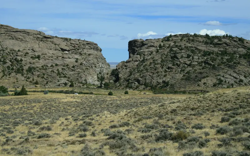 A tall rock buttress with a cleft in the center sits behind a sagebrush covered valley.
