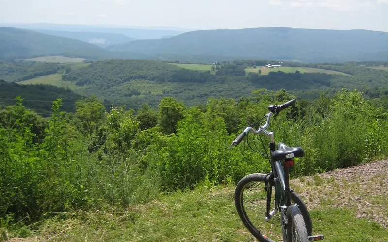 A bicycle sits on a bright summer day overlooking the rolling mountains in the distance.