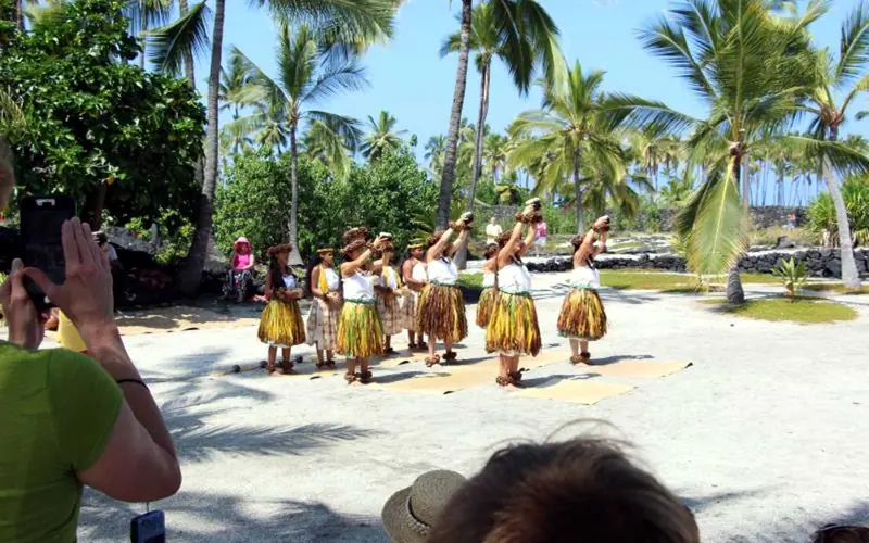 Hula dancers raise their arms to the sky in the sandy Royal Grounds.
