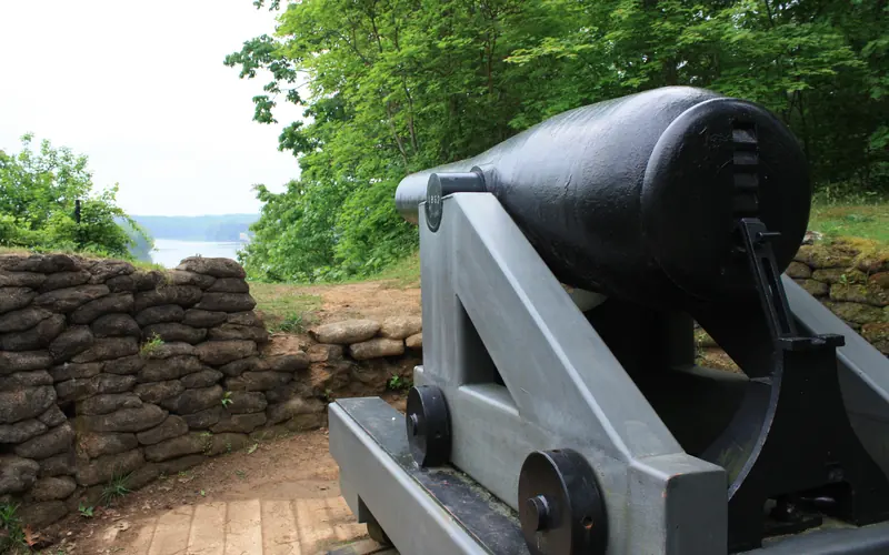 A large, black Civil War cannon overlooking a river from a high bluff.