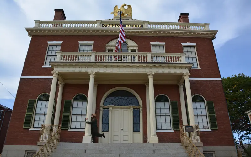 Three story red brick building with white columns has a wide staircase and golden eagle on top.