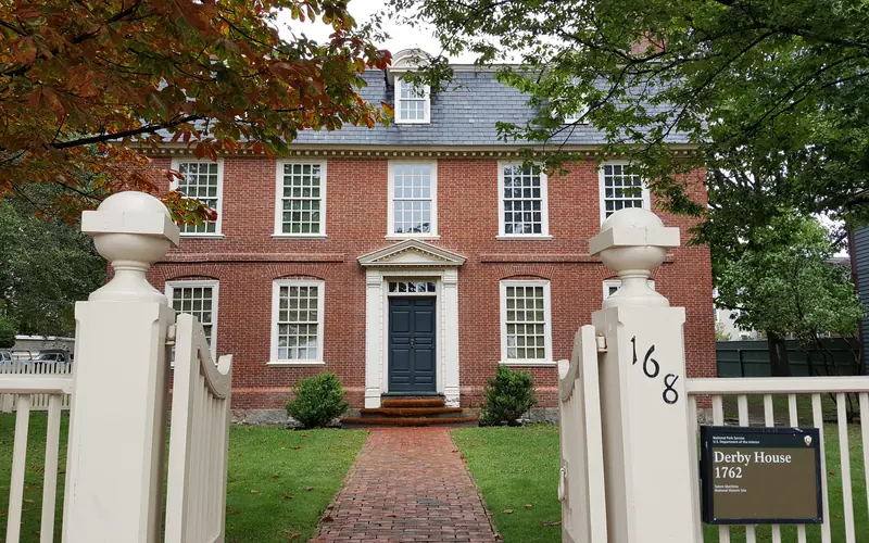 Three story red brick building with white windows and a brick pathway through grasses and trees.