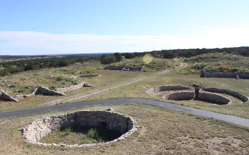 A paved path winds through the stone foundations of several old kivas.