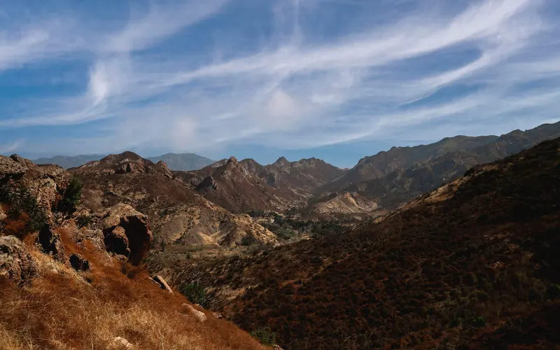 Wispy cloud covered sky over chaparral covered mountains.