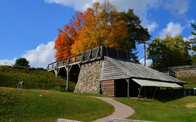 Rectangular wooden structure between orange deciduous trees and wooden bridge with walkway.