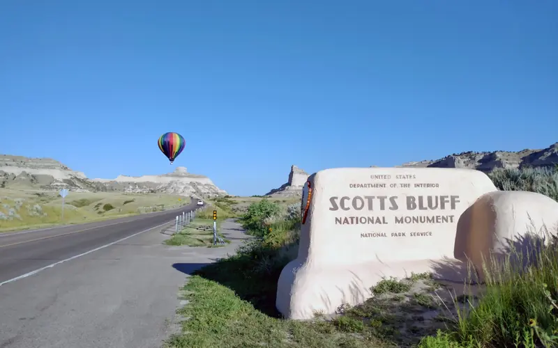 A colorful hot air balloon is seen in the distance with the Scotts Bluff entrance sign.