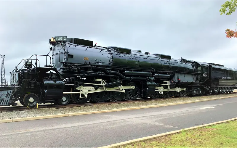 large black train stationed on a track to the left of a paved road