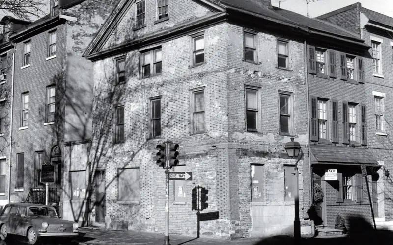 Black and white photo, circa 1960, showing a three story brick rowhouse situated on a corner lot.