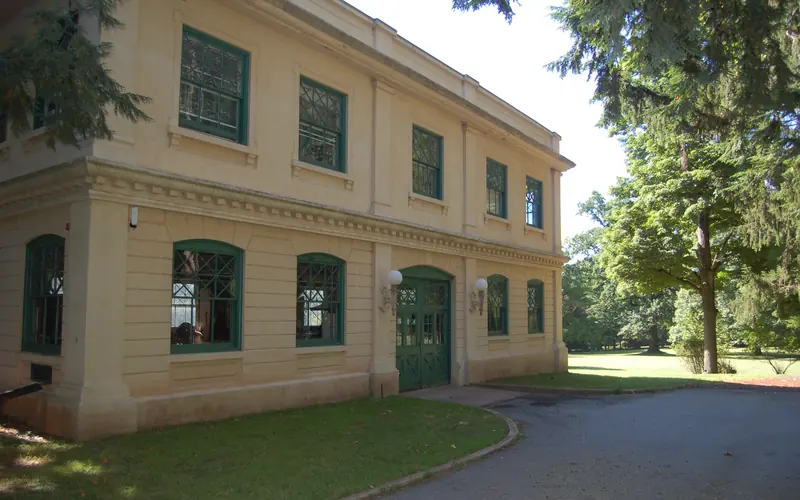 Cream colored, two story cement building surrounded by large trees