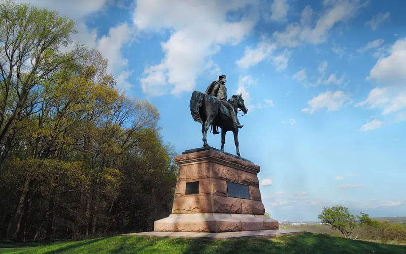 outdoors, monument, statue, man on horse, grass, trees, clouds.
