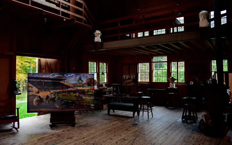 The inside of a studio with several northern windows, paintings, sculptures, and art supplies.