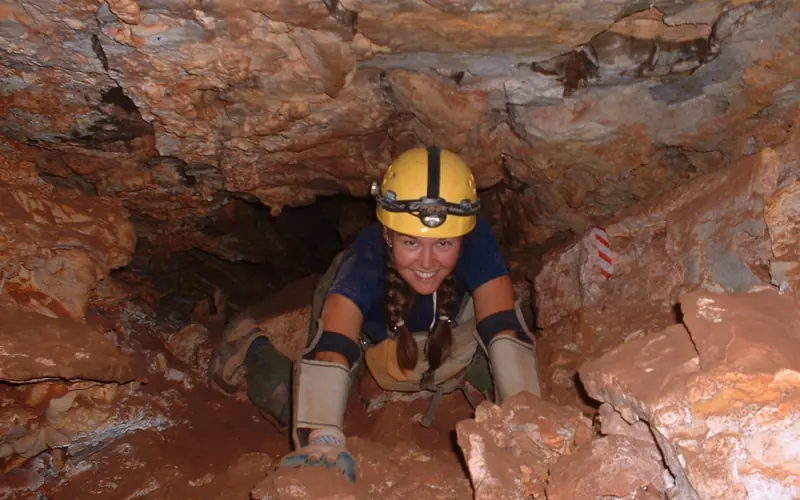 a caver with pads and helmet crawling in the cave