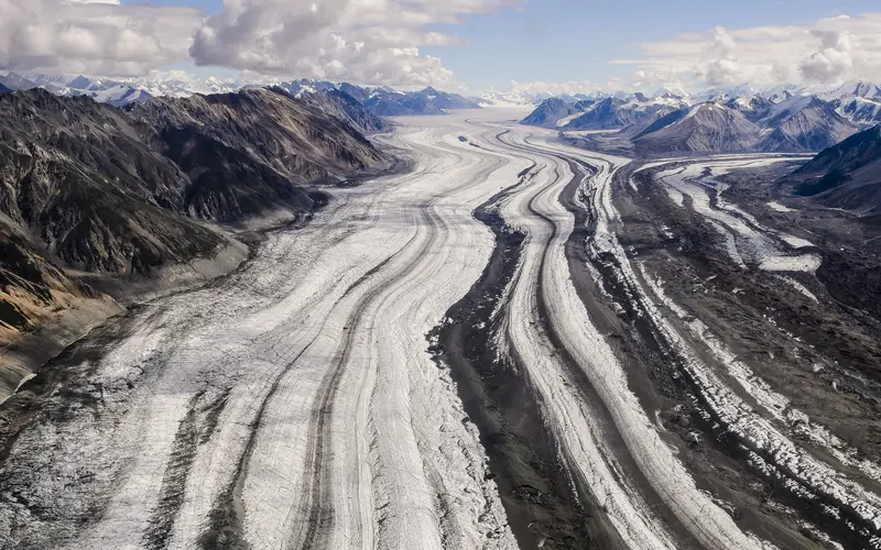 A large glacier with stripes of different colored rock nestled in between barren mountain slopes.
